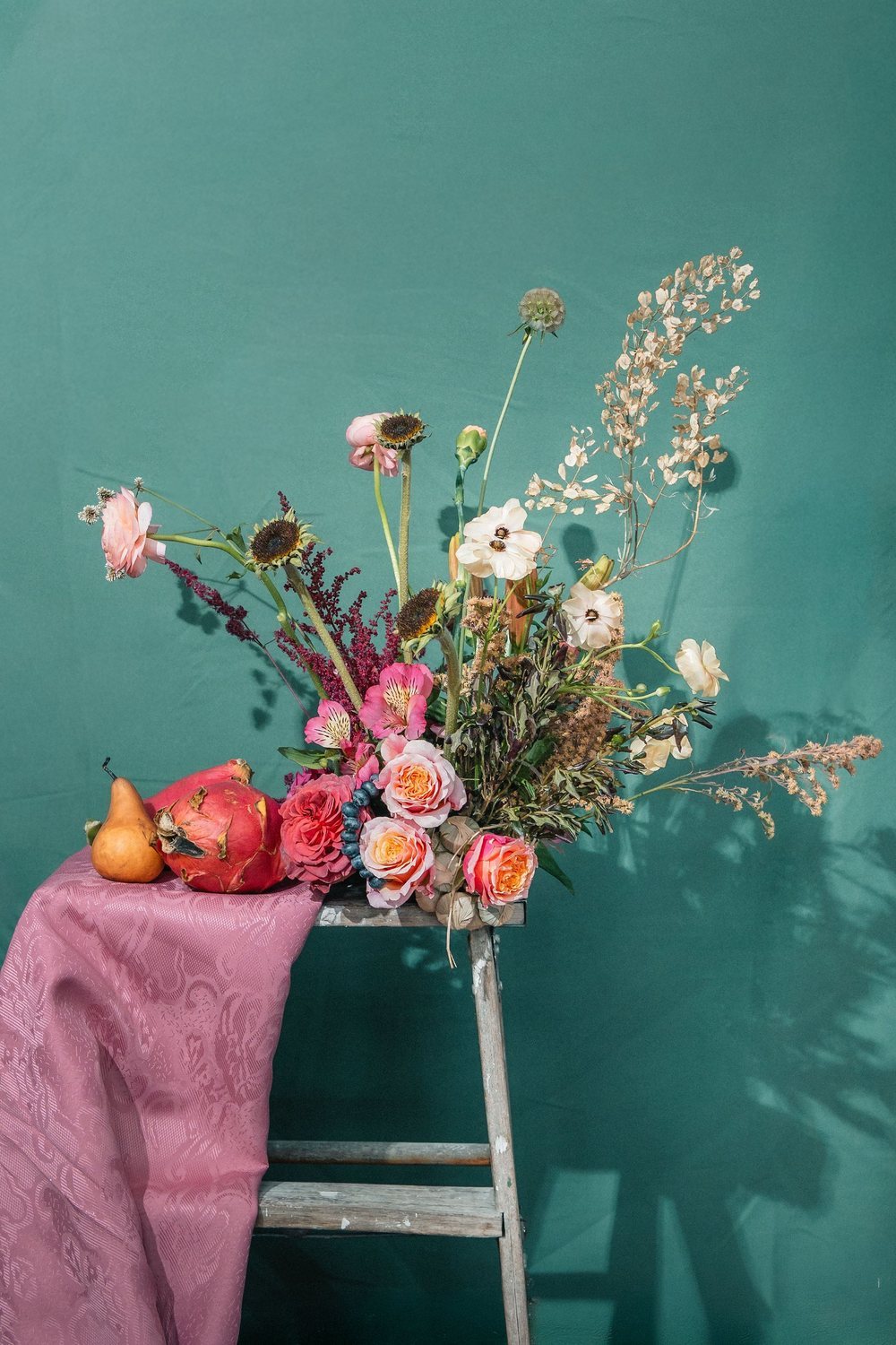 Coral and apricot garden roses with raspberry astilbe and cream ranunculus against a Transformative Teal wall